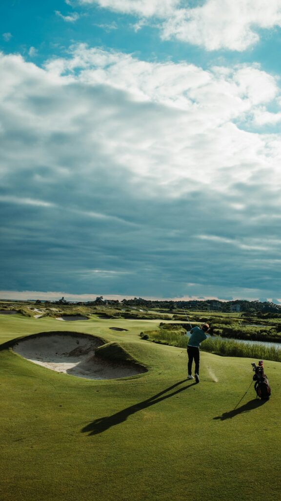 A golfer swinging a club on a green course under a cloudy sky
