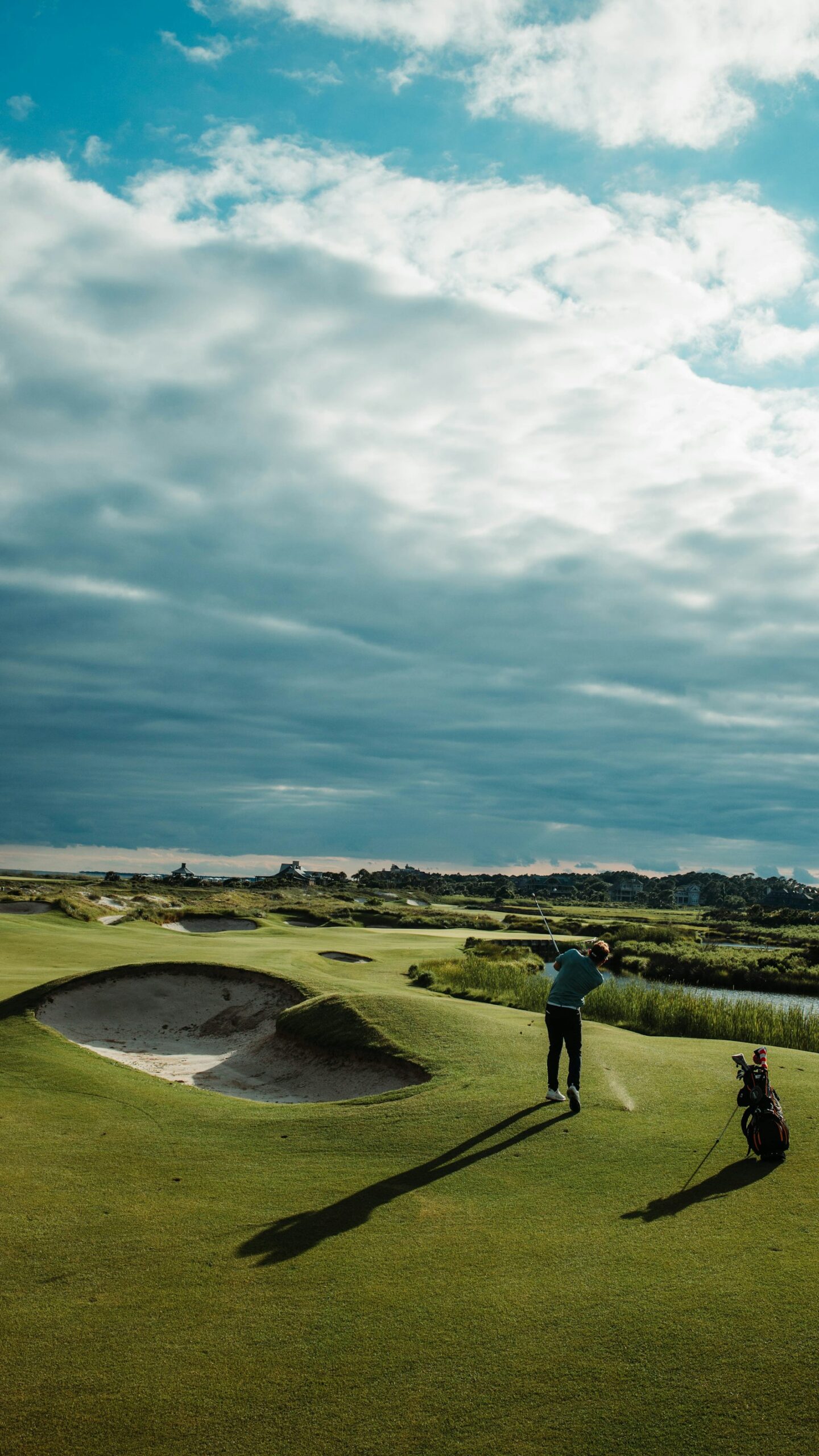 A golfer swinging a club on a green course under a cloudy sky