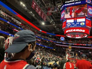 A crowd of fans standing around a basketball court in a packed arena on game night