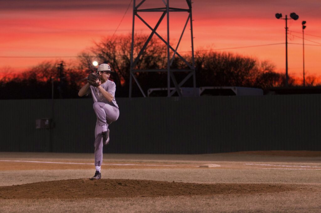 A baseball pitcher mid-delivery on the mound at sunset